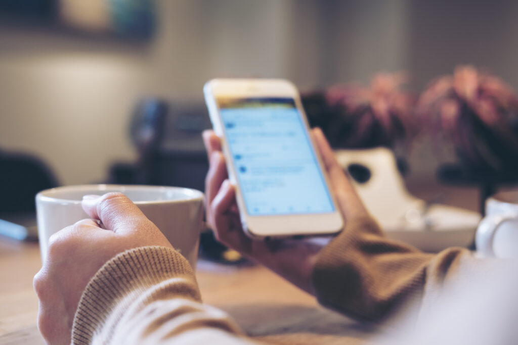 a woman's hands holding white coffee cup and mobile phone while